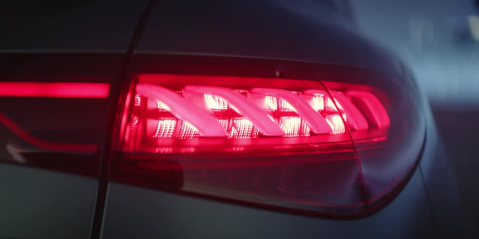 The tail light of a dark colored automobile turns on and off