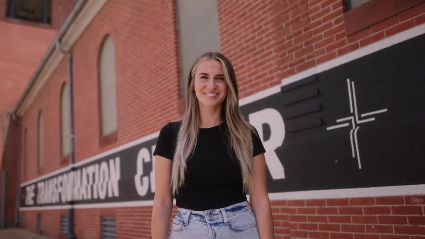 A woman with long blond hair is standing outside of a building with a smile on her face