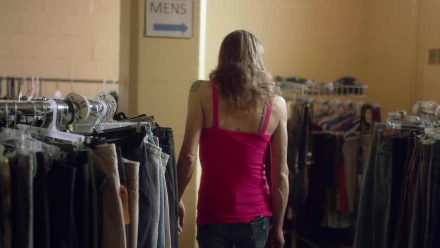 A woman is in a store shopping and looking at clothes on racks