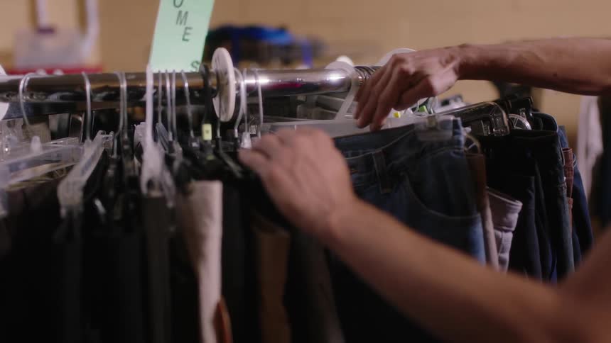 A woman is in a store shopping and looking at clothes on racks