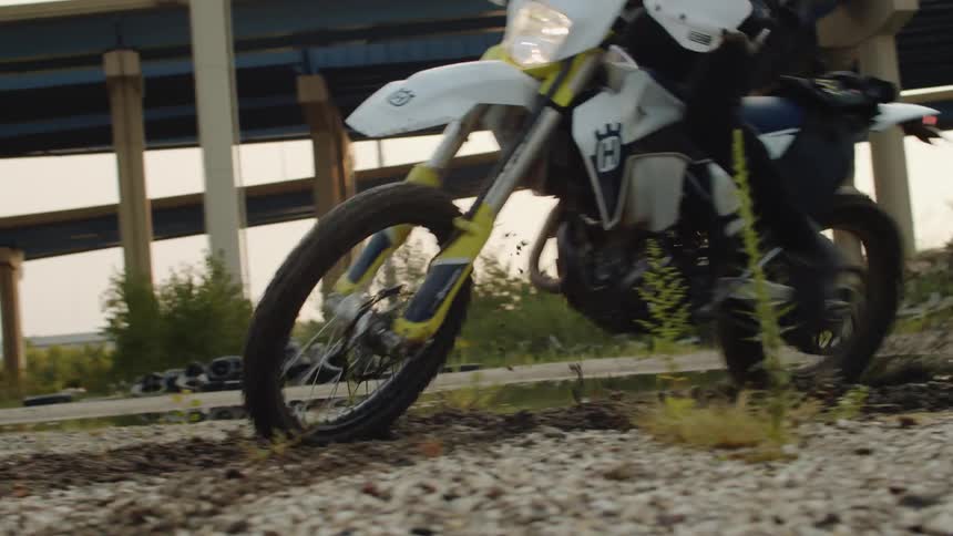 A cyclist riding a motorcycle near an underpass makes a sharp turn in the dirt
