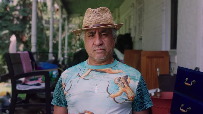 An elderly man is standing outdoors and wearing a hat
