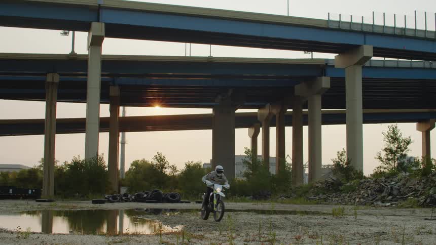 A man is riding a motorcycle under a bridge