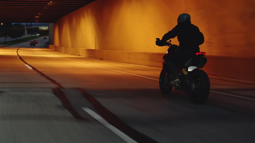 Person wearing helmet rides motorcycle along controlled access freeway at night