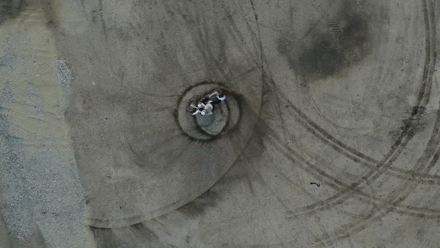 White motorcycle spins in circles and creates circles in the dirt then it rides away