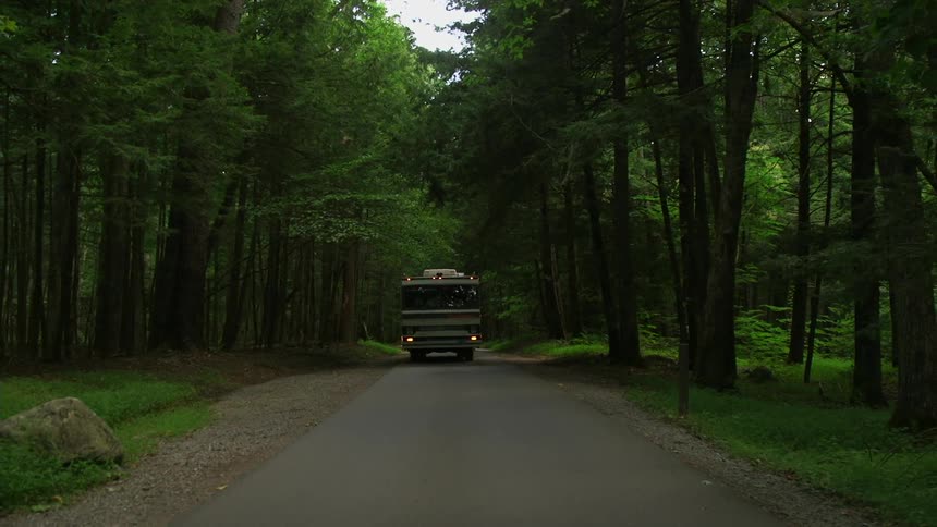 An rv drives down a wooded road