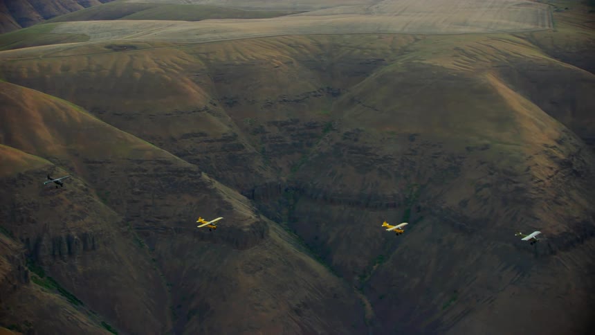 Colorful backcountry airplanes fly in formation over the slopes of the Deschutes River valley at sunrise