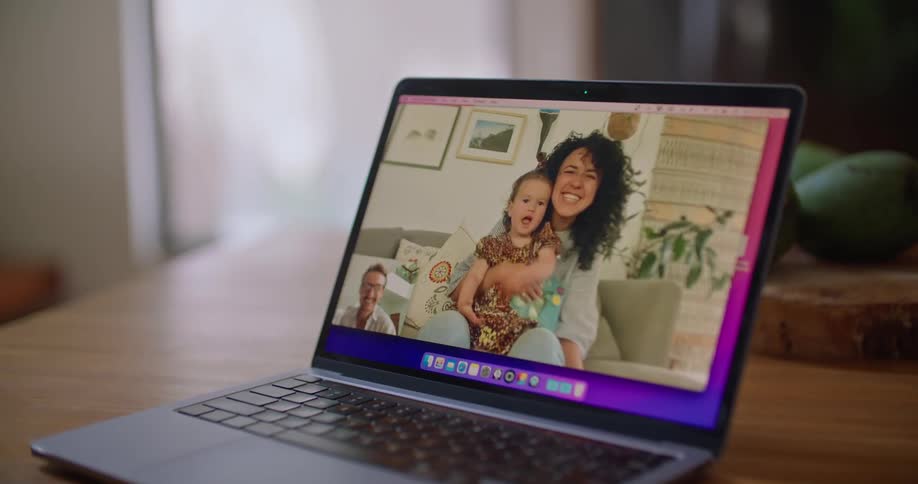 A man blows a kiss to a woman holding her baby during a video call on a laptop