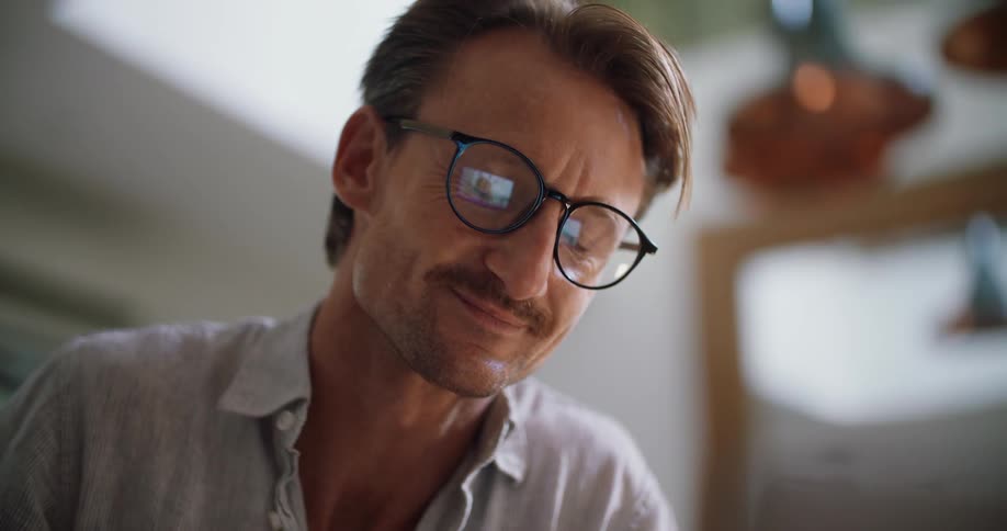 Man talks then blows a kiss at the laptop reflected in his eyeglasses