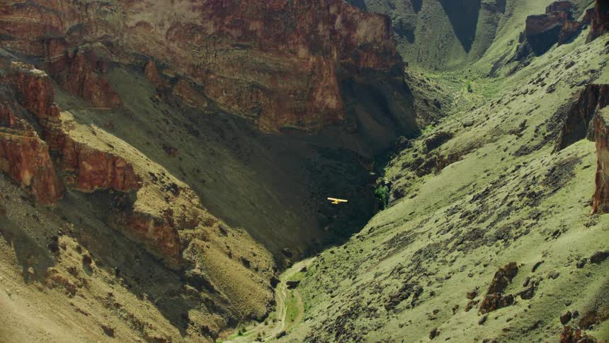 A small Carbon Cub airplane flies in the valley of a canyon in the desert