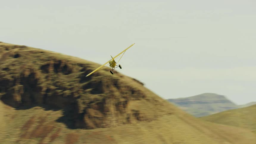 A small yellow backcountry Carbon Cub airplane is flying near mountains in the desert