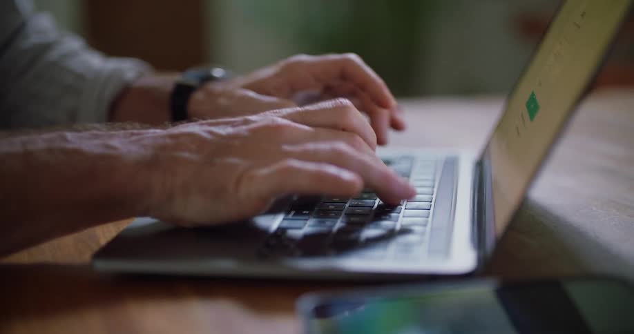 A man is sitting at a table typing on a laptop computer keyboard