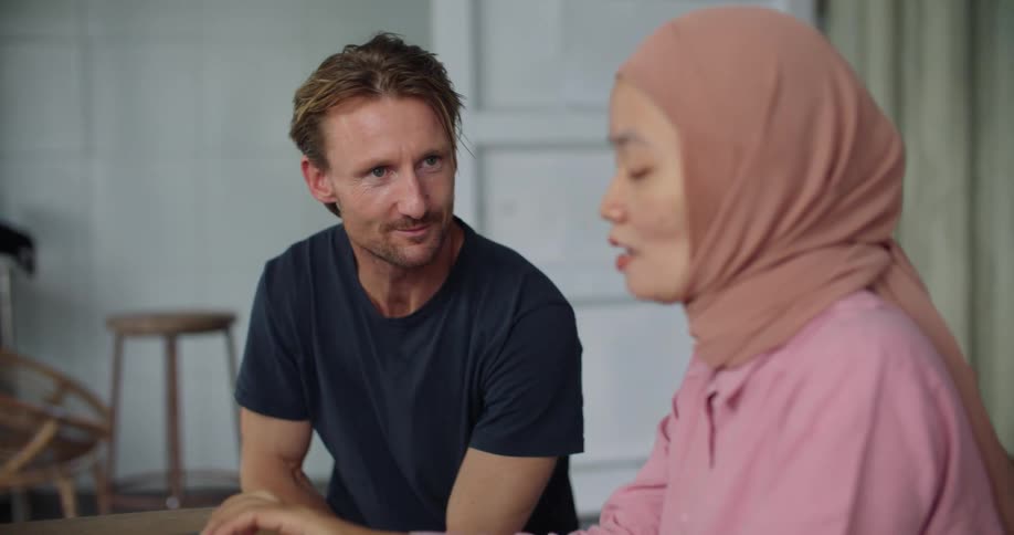 A man talking to a woman wearing a muslim shayla while sitting on a room at home