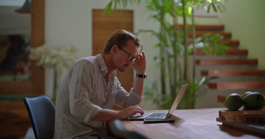 Man sits at large table at home and works on laptop