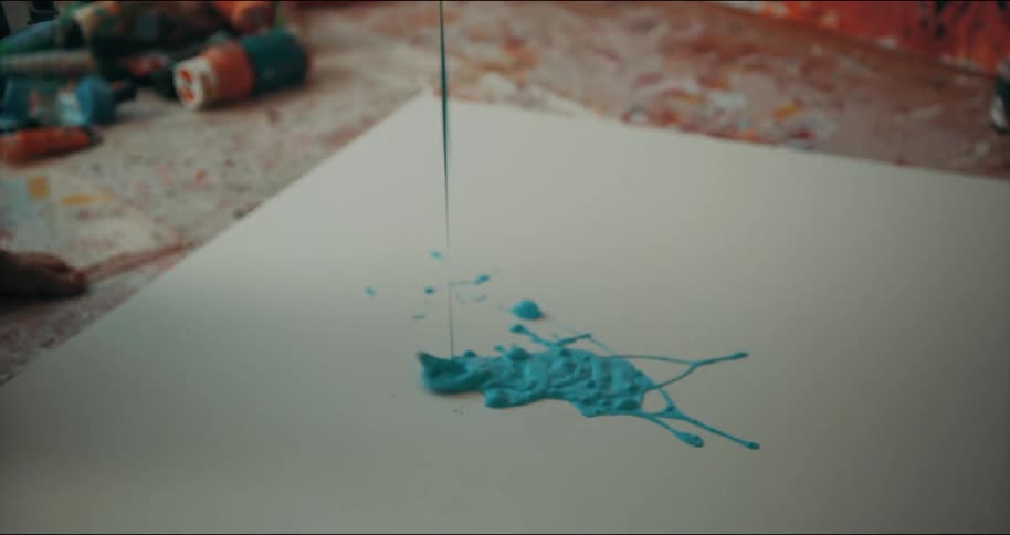 An artist is pouring paint onto a canvas on the floor