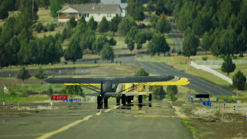Small planes move on a runway in a residential area and there are houses nearby among many trees