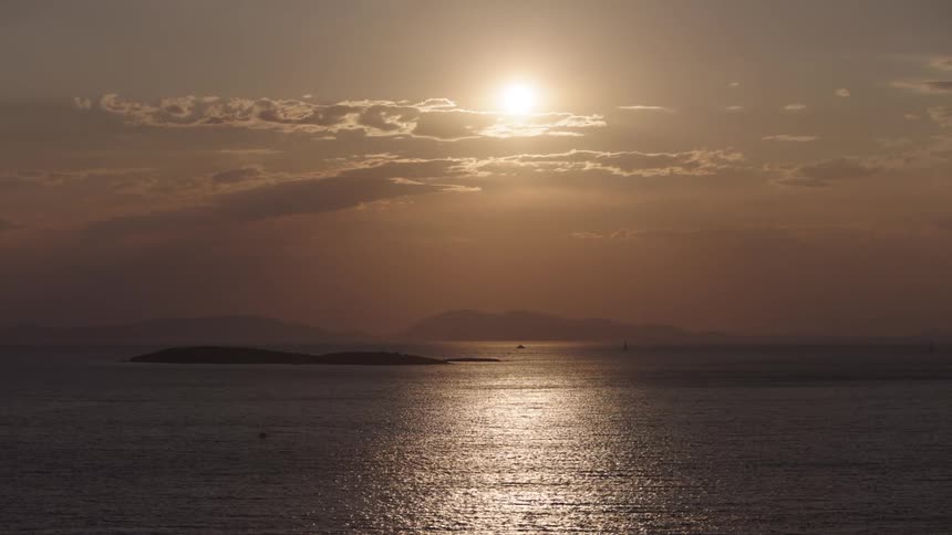 Sunlight shines on the water and it sparkles as it ripples and waves under an orange sky and there are mountains in the distance