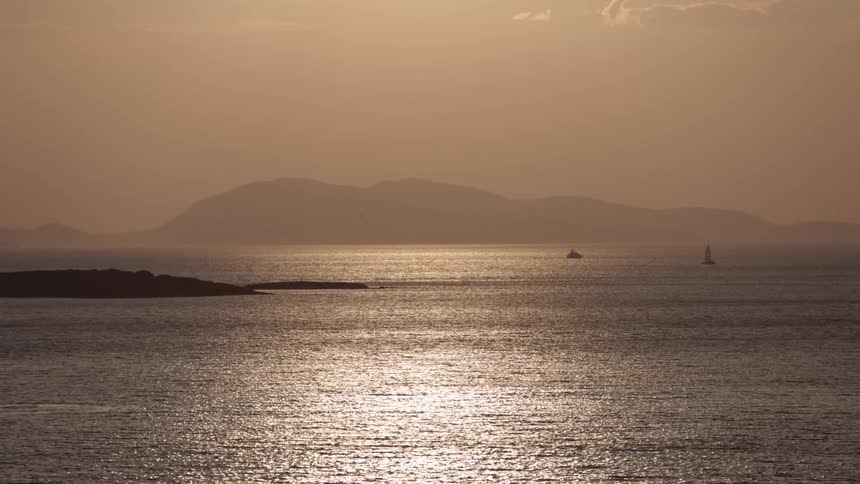 Calm and serene scene of the sun reflecting on the ocean with distant mountains in the horizon