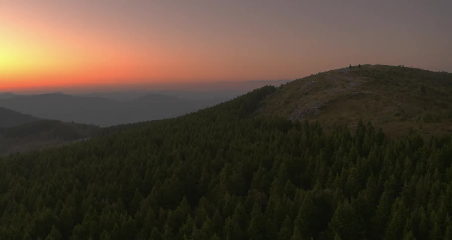 Forested mountains under a red sky and mountains are on the horizon