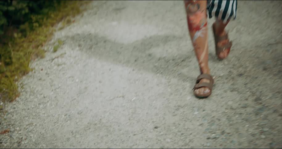 A woman covered in paint walks down a sidewalk past a passenger train