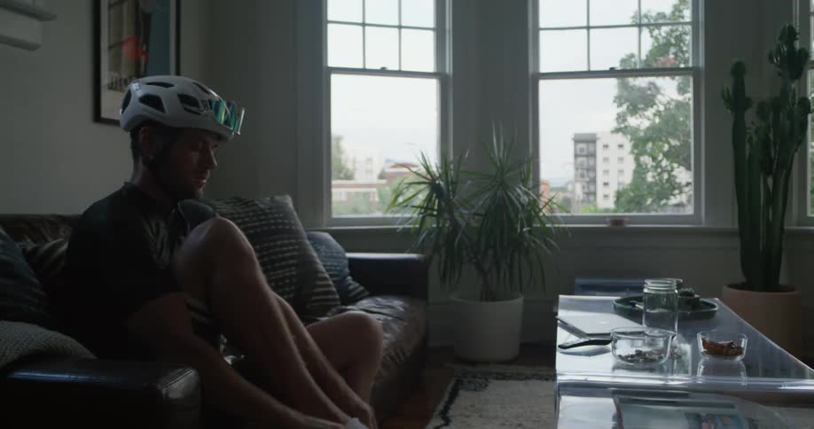 A cyclist puts on his socks while sitting on a sofa in a living room during the day