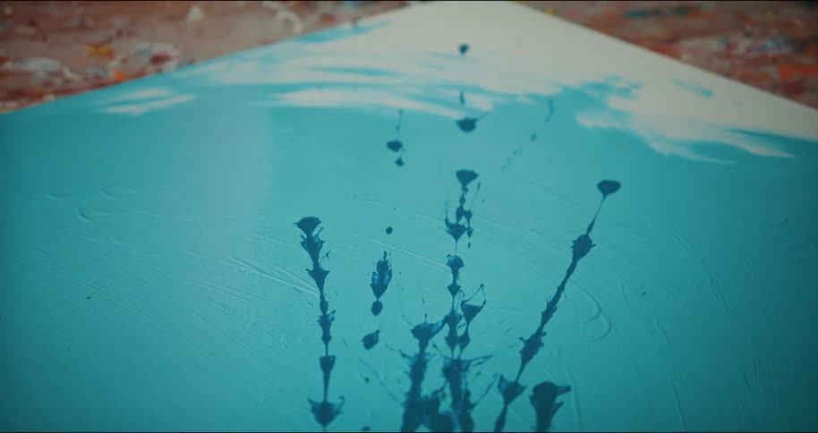 Artist shakes blue paint onto a canvas