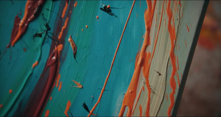 Orange paint drips down a canvas being painted outdoors