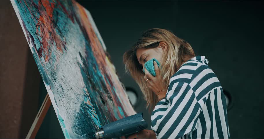 An artist holds a rag to her face before using a power tool to dry her painting