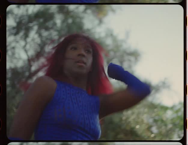 Female dancer with red hair blue top and sports pants dances on lawn in public park