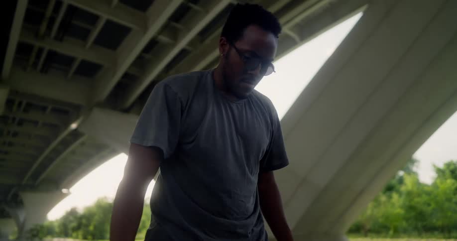 Man wearing sunglasses stretches out under a highway at daytime