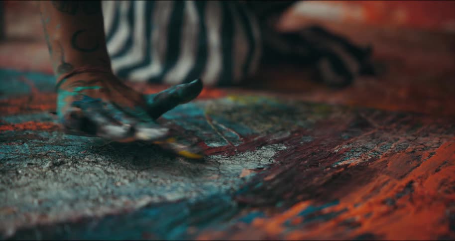 An artist spreads paint on her canvas with her paint covered fingers