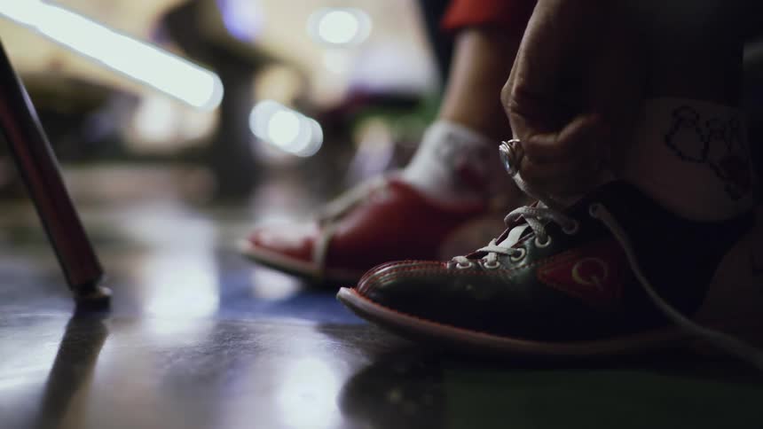 Close up of a person tying up the white laces on colorful bowling shoes