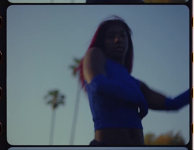 Female dancer with red hair blue top and sports pants dances on lawn in public park