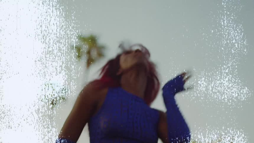Footage with white scratches of a young woman with red hair dances in front of palm trees