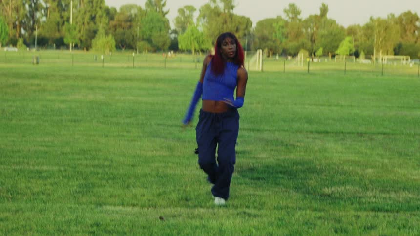 Black woman wearing long blue gloves and a matching blue top dances on a grassy field
