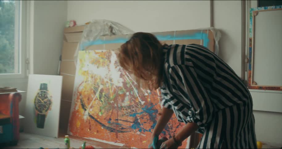 Female artist spreads paint from container onto canvas lying on the floor
