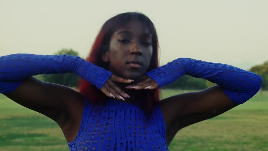 A woman dances by moving her arms while standing in a park