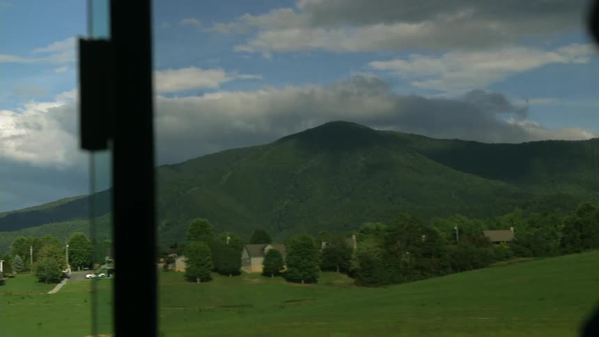 Outside the window of a moving vehicle are hills covered with grass