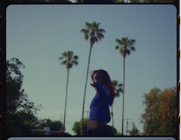 Young woman with red hair dances in front of palm trees caught on vintage film