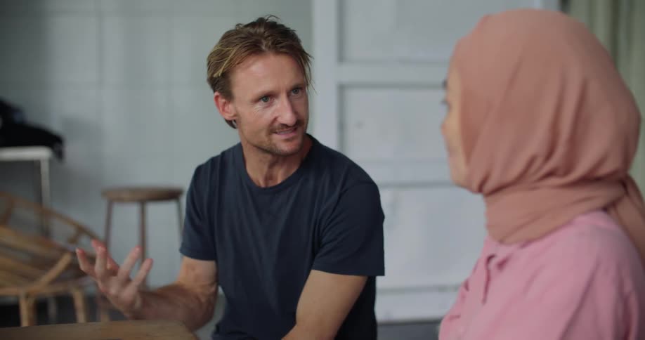 A man talks to a woman using a laptop at a table indoors during the day
