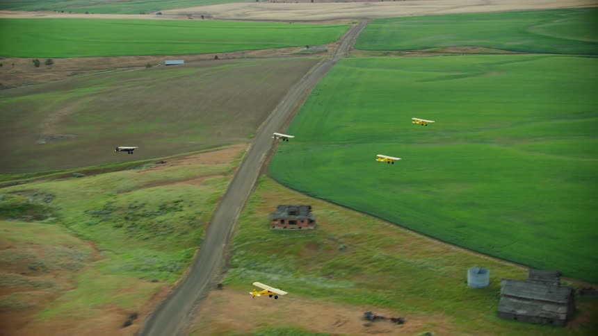 Five airplanes fly together over big green pastures filled with roads homes and barns in a large area of land