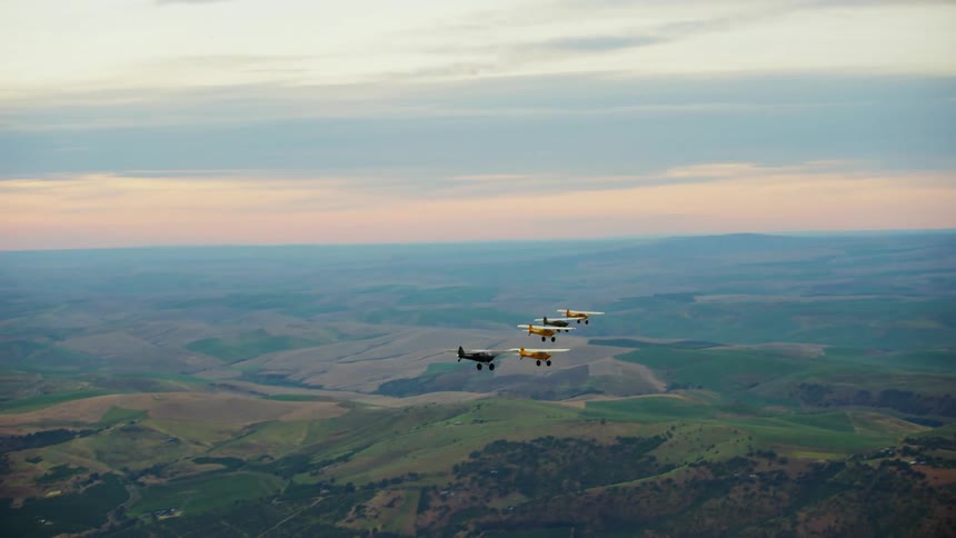 Colorful propeller backcountry airplanes fly in formation over the slopes of a mountain in the morning hours