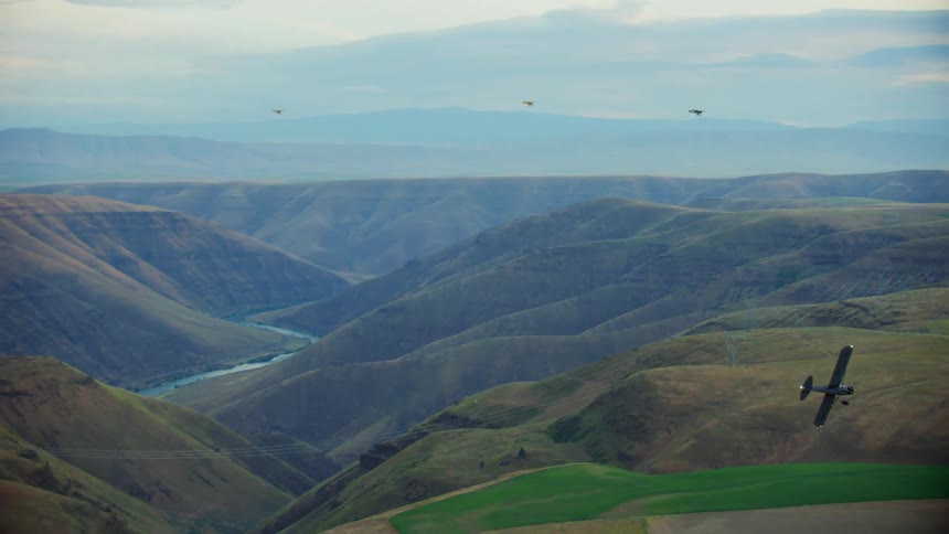An airplane tips its wings and turns reversing direction over hills and stream