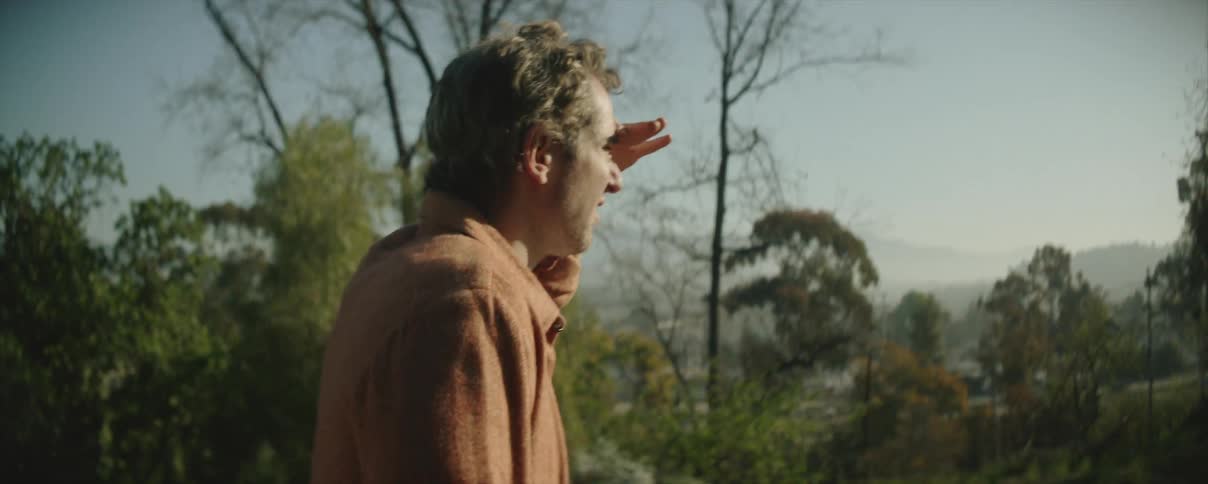 A man is outside walking near trees and traffic is moving on a highway down the hill