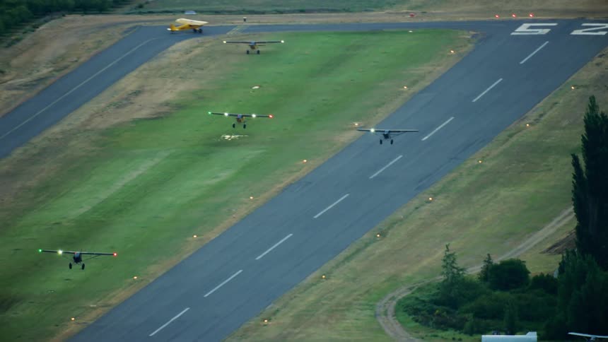 A group of small backcountry airplanes take off from a runway during the early morning light