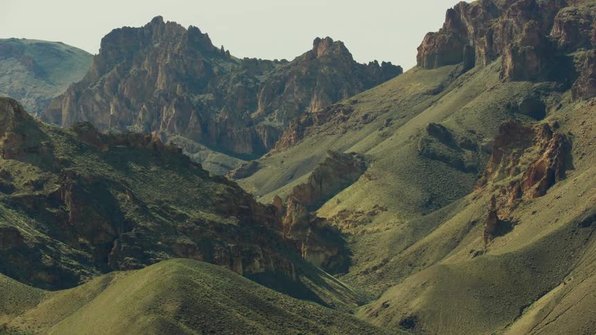 Aerial view of the gentle slopes covered in grass on the sides of a rocky mountain range