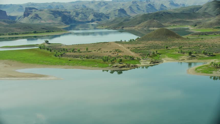 The clear calm lake surface reflects the blue sky trees and hills