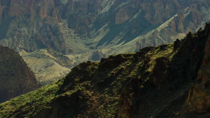 Aerial view of the gentle slopes of a small valley covered in grass on the sides of a rocky mountain range