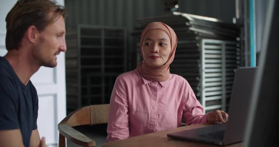 Man points to a laptop as he sits at a desk talking with a middle eastern woman