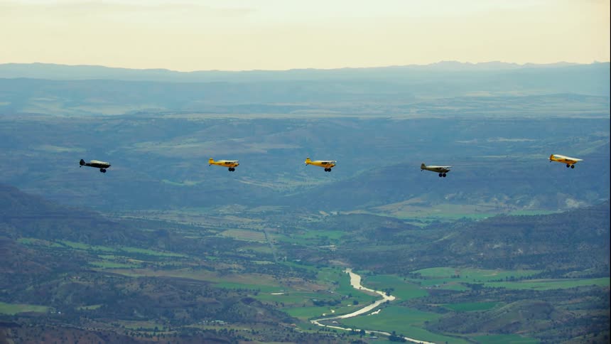 Five small backcountry airplanes fly in a line over the valley between the mountains